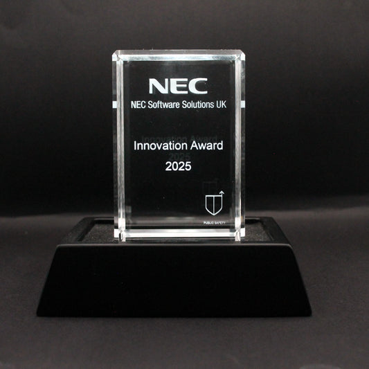 Clear glass award with NEC branding on a black stand against a dark background