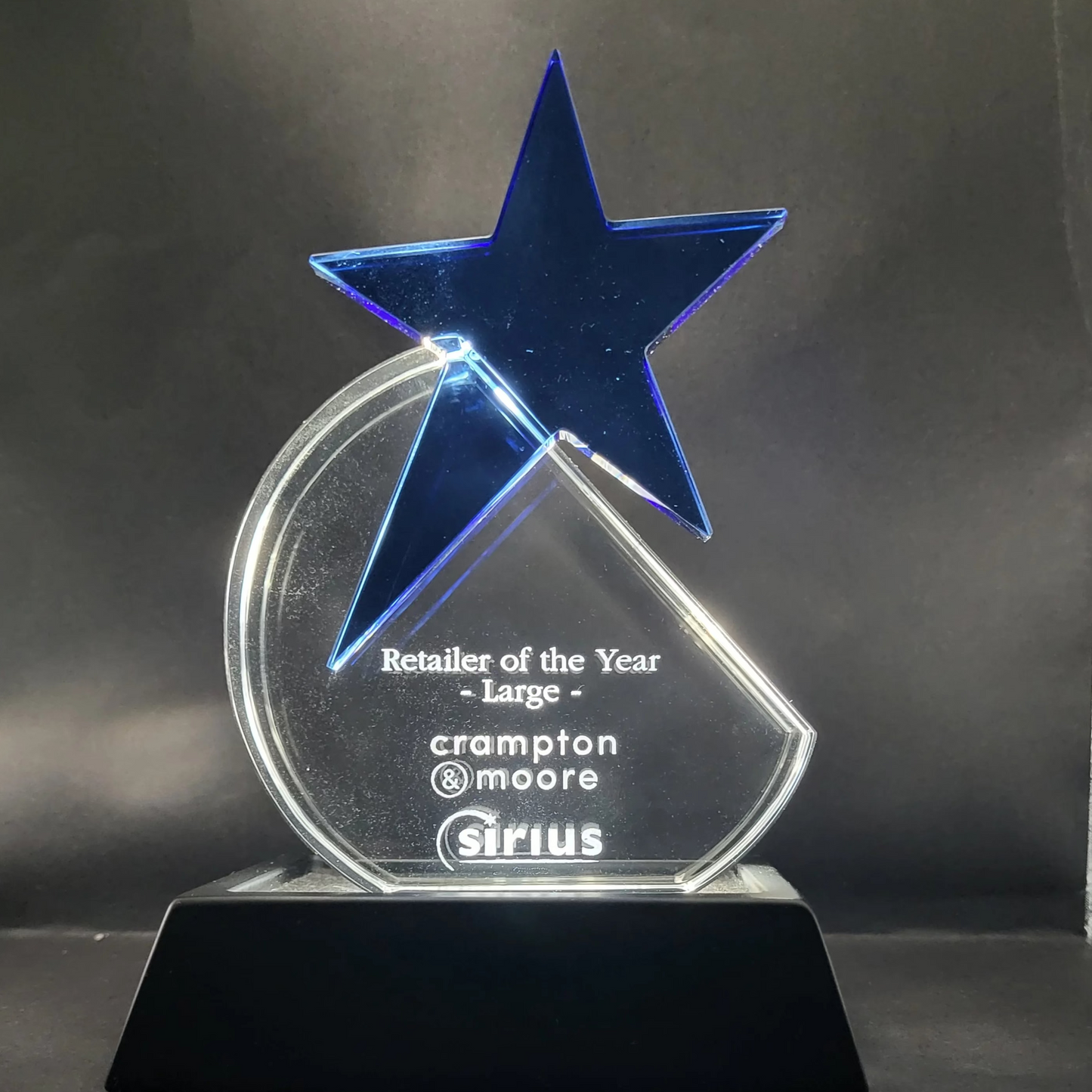 Glass CrystalAwards trophy with a blue star and clear base on a dark background